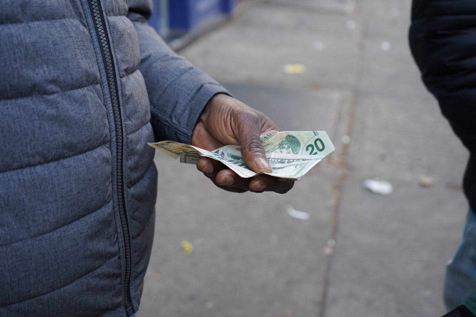 A person holding money in their hand on the sidewalk.